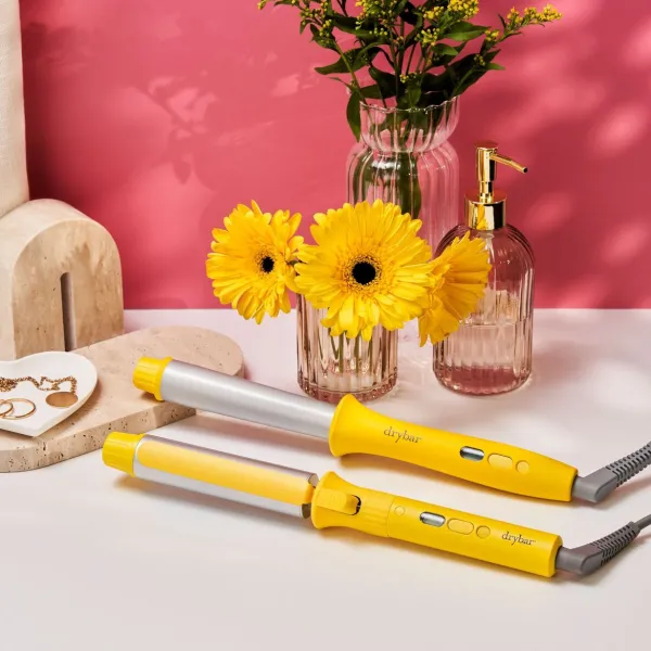 Drybar matu veidošanas ierīces dzeltenā krāsā novietotas blakus ziediem un dekoratīviem interjera elementiem.