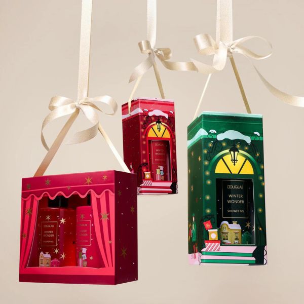 Trīs dekoratīvas dāvanu kastītes, kas atgādina mājiņas, karājas uz plānām baltām lentītēm; kastītes ir apzīmētas ar "Douglas Winter Wonder Shower Gel".