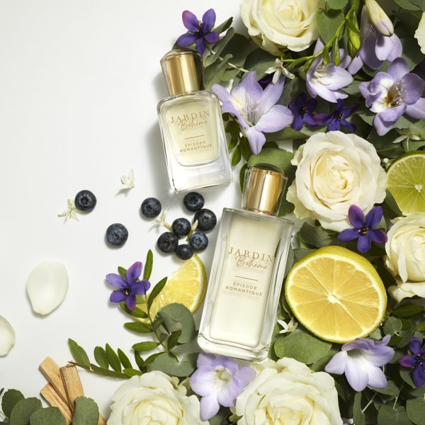 "Jardin Bohème Épisode Romantique smaržu pudeles, novietotas starp baltām un violetām ziediem, mellenēm un citronu šķēlītēm svaigā un elegantā kompozīcijā."