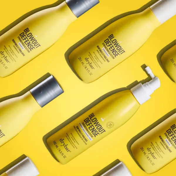 Drybar Blowout Defense matu kopšanas produktu kolekcija uz dzeltena fona.