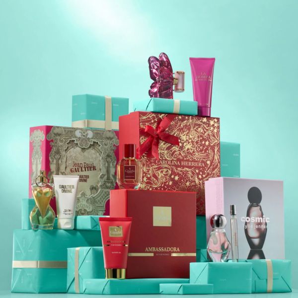Dovanų rinkinys su įvairiais kvepalais ir kosmetikos gaminiais, išdėliotas ant šviesiai mėlynų dovanų dėžučių; rinkinyje yra „Jean Paul Gaultier“ ir „Carolina Herrera“ produktai